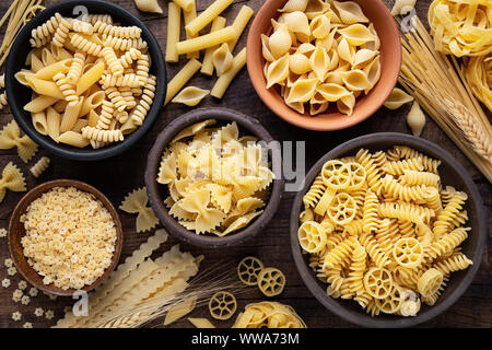 Varietà di tipi e sshapes secca di pasta italiana in ciotole contro scuri in legno rustico sfondo