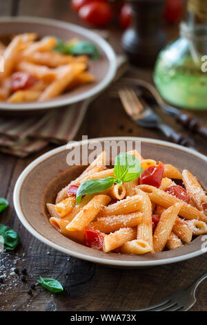 Piatto di pasta penne con cherry di salsa di pomodoro, basilico e parmigiano grattugiato - Pasta al pomodoro. Servita in piatti rustici di una cena per due Foto Stock