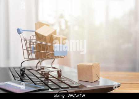 Shopping online concetto. Carrello spesa, piccole scatole, laptop e una carta di credito sulla scrivania Foto Stock