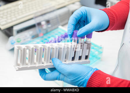 Medico mano prendendo un tubo contenente il campione di sangue da una cremagliera con macchine di analisi in laboratorio di background tecnico / azienda sangue test in provetta nella ricerca Foto Stock