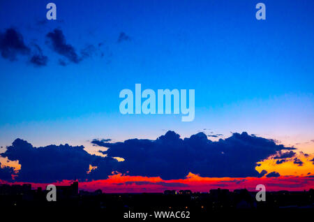 New Scenic 5 posti è vista sul bel cielo azzurro con soffici nuvole al tramonto e il paesaggio urbano in distanza. Foto Stock