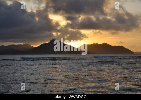 Seychelles tramonto dietro l'Isola di Praslin. Vista da La Digue Island. Foto Stock