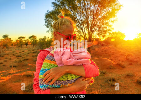 Donna turistica holding ed kissing kangaroo joey alla luce del tramonto in outback australiano. Interagire con graziosi kangaroo orfano. Marsupiale australiano in Foto Stock