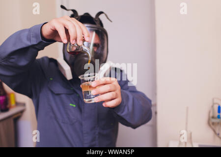 Il Tecnologo in bianco tuta protettiva con retina per capelli e maschera e lavorando in cibo e bevanda fabbrica. L'uomo specialista controllo bottiglie per prodotto di bevanda Foto Stock