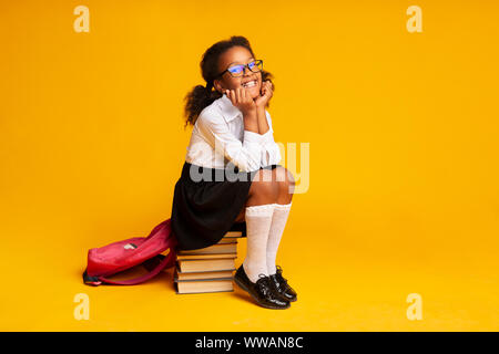 Sorridente livellatrice prima ragazza seduta sulla pila di libri in Studio Foto Stock