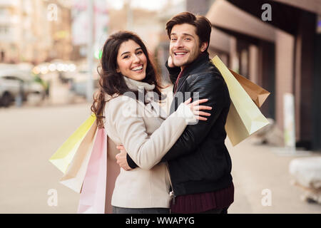 Amare giovane con le borse della spesa che abbraccia all'aperto Foto Stock