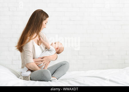 Giovane madre mentre tiene il suo figlio neonato, Lulling baby a letto Foto Stock