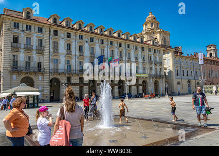 I bambini giocano nelle fontane di Piazza Castello, una piazza importante della città in una calda giornata estiva a Torino Foto Stock