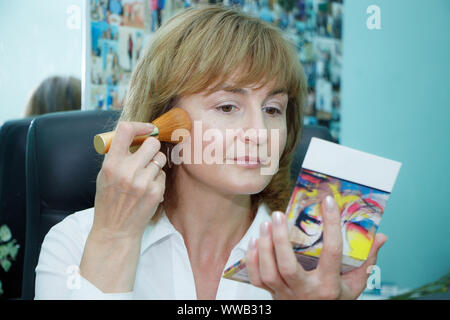 Close up di una matura donna bionda facendo viso trucco, il fuoco selettivo Foto Stock