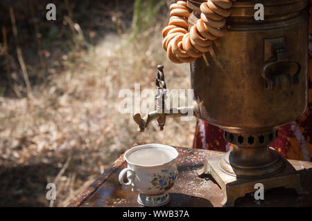 Vintage samovar bronzo la combustione del legno e la coppa sul tavolo arrugginita all'aperto, la preparazione di acqua per il tè di birra, il fuoco selettivo Foto Stock