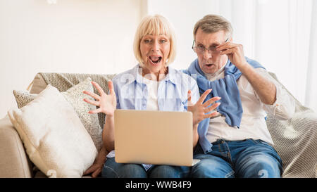 Sorpreso Coppia matura vincere online auction, utilizzando laptop Foto Stock