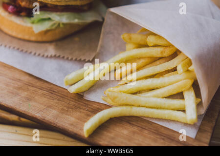 Freschi e saporiti hamburger e patatine fritte su un tavolo di legno. le patatine e salsa barbecue sul piatto di legno. street food Burger e patate fritte. Alimenti dannosi per la salute Foto Stock