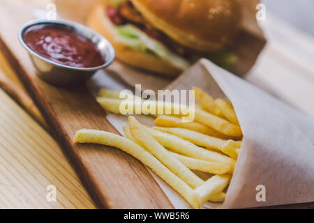 Freschi e saporiti hamburger e patatine fritte su un tavolo di legno. le patatine e salsa barbecue sul piatto di legno. street food Burger e patate fritte. Alimenti dannosi per la salute Foto Stock