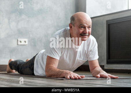 Senior uomo ispanico facendo variazione del cobra pongono in una sala luminosa Foto Stock