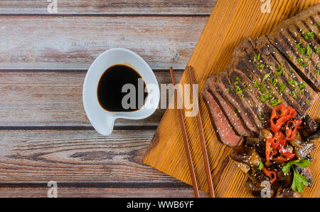 Il coreano grigliate di carne e funghi, Salsa di soia, sul tagliere con bacchette. Foto Stock