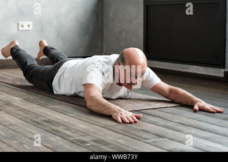 Senior uomo ispanico facendo la variazione Shalabhasana sull esercizio mat. Foto Stock