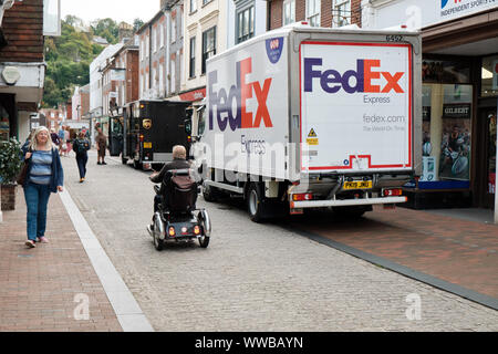 Fedex e UPS furgoni parcheggiati illegalmente nella zona pedonale della città mentre una ridotta mobilità persona va da sulla strada di ciottoli. Lewes Regno Unito Foto Stock