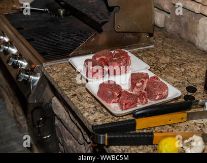 Bistecche condita e preparata per la cottura alla griglia su un patio esterno Foto Stock