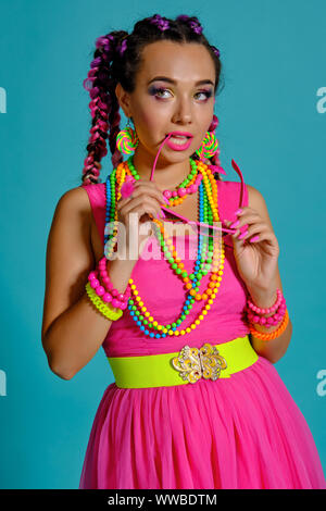 Bella ragazza con un multi-colore trecce acconciatura e luminoso per il make-up, che pongono in studio contro uno sfondo blu. Foto Stock