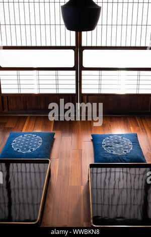 Tradizionale Giapponese casa machiya ryokan ristorante con nero laccato tavolo in legno con cuscini cuscino, lampada e scorrimento delle porte della carta con naturale Foto Stock