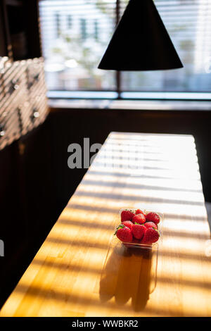 Tradizionale Giapponese del dessert confezionato box di plastica contenitore di plump costoso fragole di legno sul tavolo da cucina, Lampada illuminata da una finestra luminosa Foto Stock