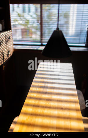 Giapponese tradizionale cucina in legno tavolo con lampada illuminata da una finestra luminosa luce solare luce e ombre Foto Stock