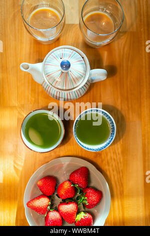 Flat top view Green Tea Cups e fragole sulla piastra con tradizionale giapponese Sencha tè verde dalla teiera sul tavolo di legno in cucina Foto Stock