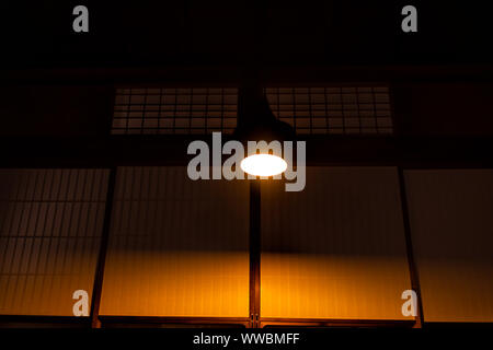 Angolo basso cercando la vista del soffitto con lampada illuminata al tradizionale giapponese casa machiya ryokan ristorante con carta di scorrimento porte al buio ni Foto Stock