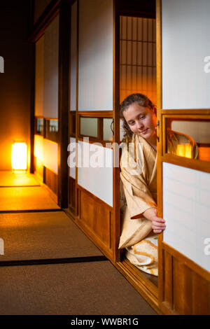 Tradizionale casa giapponese o ryokan camera con gaijin caucasian donna in kimono, dei tabi calzini apertura porte scorrevoli di carta shoji seduti sul tatami flo Foto Stock