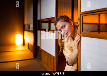 Tradizionale casa giapponese o ryokan con gaijin caucasian donna in kimono, dei tabi calzini apertura porte scorrevoli di carta shoji seduti sul tatami piano Foto Stock