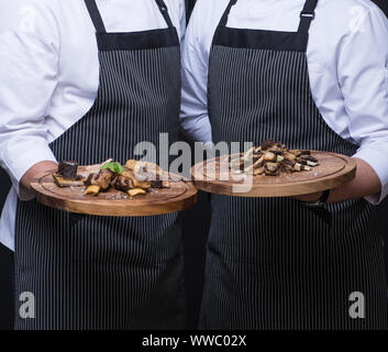 Due camerieri di servire un piatto di carne su un vassoio in legno Foto Stock