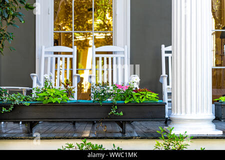 La vecchia strada giardino storico distretto di New Orleans, in Louisiana con patio giardino piante verdi fiori, bianco antebellum colonna e sedie a dondolo da ma Foto Stock