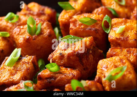 Il Paneer Manchurian o Paneer 65 in coppa a nero lo sfondo di calcestruzzo. Il Paneer Manchurian è indiano cucina cinese il piatto con il panner formaggio, pomodori, su Foto Stock