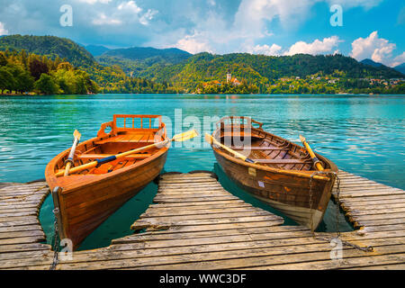 Carino in legno barche a remi ancorata al molo sul lago di Bled. Famoso Pillgrimage chiesa e la piccola isola di background, Bled, Slovenia, Europa Foto Stock