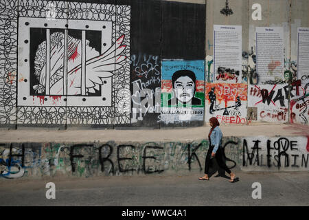 Una donna Palestinese passeggiate lungo la barriera di separazione o parete spruzzata con graffiti di slogan da turisti alla periferia della città di Betlemme in central West Bank. Territori palestinesi, Israele Foto Stock