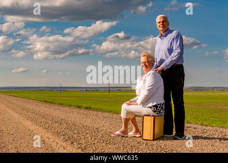 Coppia senior con valigia vintage su un paese strada di ghiaia in Saskatchewan, Canada. Adventure Concept. Guardando al futuro concetto Foto Stock