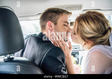 Vista posteriore della sposa attraente in velo nuziale e sposo baciare in auto Foto Stock