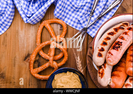 Il tedesco salsicce alla griglia. Tradizionale pasticceria e brezel per la festa della birra. Sfondo di legno e arredamento. Vista da sopra Foto Stock