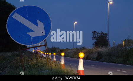 Roadworks coni lampeggiante sulla autostrada del Regno Unito durante la notte con il traffico passante Foto Stock