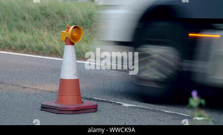 Roadworks cono lampeggiante sulla autostrada del Regno Unito durante la notte con il traffico passante Foto Stock