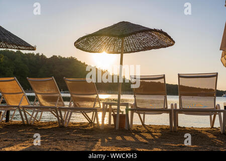 Svuotare i lettini e ombrelloni sulla mattina, dal mare. Spiaggia di sabbia in un lussuoso hotel resort vicino al mare. Bel mattino seascape. Bodrum, Turchia Foto Stock