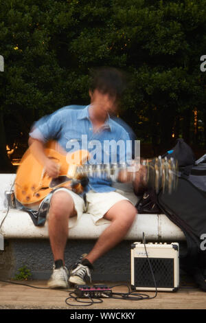 L'uomo giapponese degli anni '20 o '30, indossando una camicia in denim, suona una chitarra elettrica gialla a Yoyogi Park, Shibuya, Tokyo, su una panchina. Foto Stock