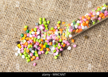 Palline di plastica .del colorante polimerico in tubi di prova su sfondo grigio. Granuli di plastica dopo la trasformazione di rifiuti di polietilene e polipropilene. Foto Stock