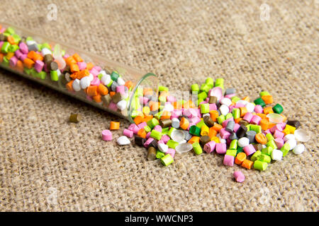 Palline di plastica .del colorante polimerico in tubi di prova su sfondo grigio. Granuli di plastica dopo la trasformazione di rifiuti di polietilene e polipropilene. Foto Stock