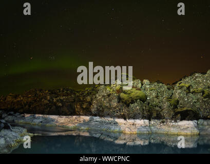 Luci del nord e riflettendo le rocce in acqua termale Foto Stock