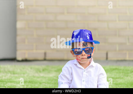 Grave ragazzo australiano indossando occhiali da sole e cappello seduti su erba om cortile anteriore durante l'Australia Day celebrazione Foto Stock