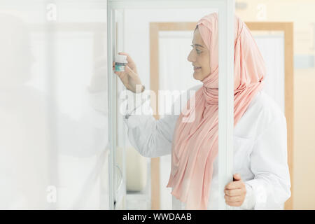 Vista laterale ritratto di donna mediorientale mettendo pillole nel gabinetto mentre lavorava come infermiera in clinica medica, spazio di copia Foto Stock