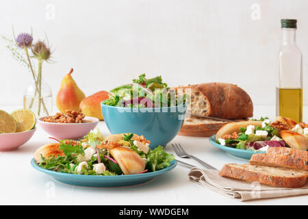 Bianco tavolo in legno di noce con insalata di pere caramellate e formaggio feta. Turquise piatti con insalata, fette di twisted Il pane svizzero con olive, limets Foto Stock