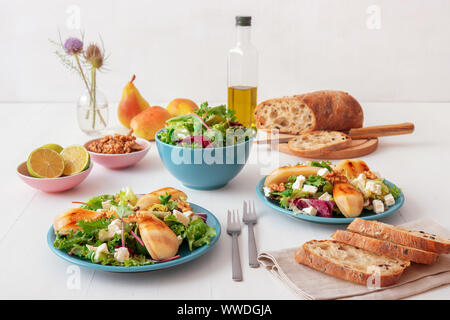 Bianco tavolo in legno di noce con insalata di pere caramellate e formaggio feta. Turquise piatti con insalata, fette di twisted Il pane svizzero con olive, limets Foto Stock