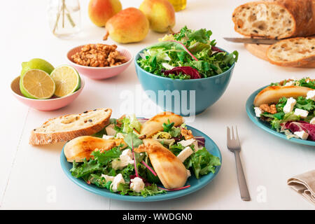 Bianco tavolo in legno di noce con insalata di pere caramellate e formaggio feta. Turquise piatti con insalata, fette di twisted Il pane svizzero con olive, limets Foto Stock